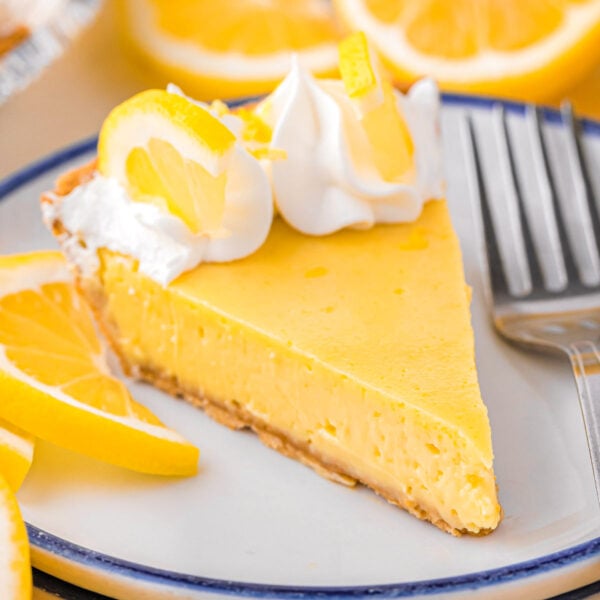 A slice of lemon pie on a stack of white plates.
