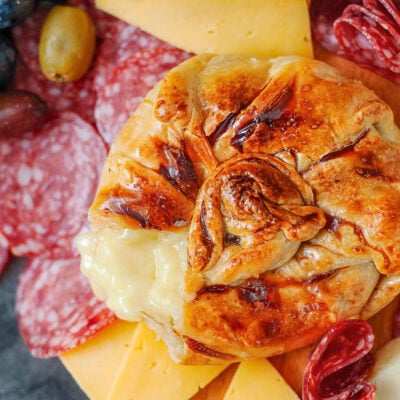 Honey baked brie wrapped in puff pastry. Salami and cheese are on the platter with the brie.
