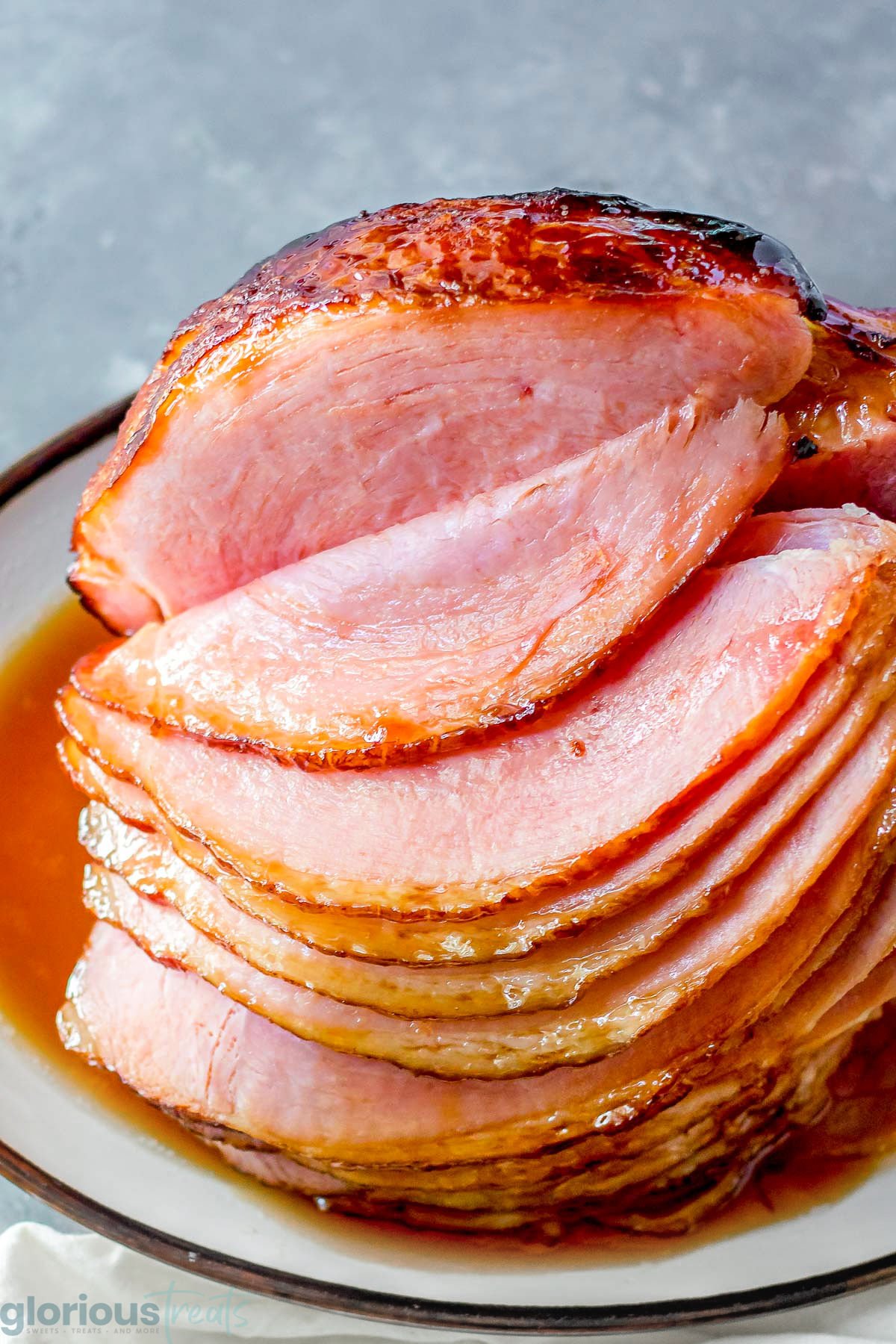 A ham on a white serving platter, with part of the ham cut into slices and the glaze glistening on top of the ham.