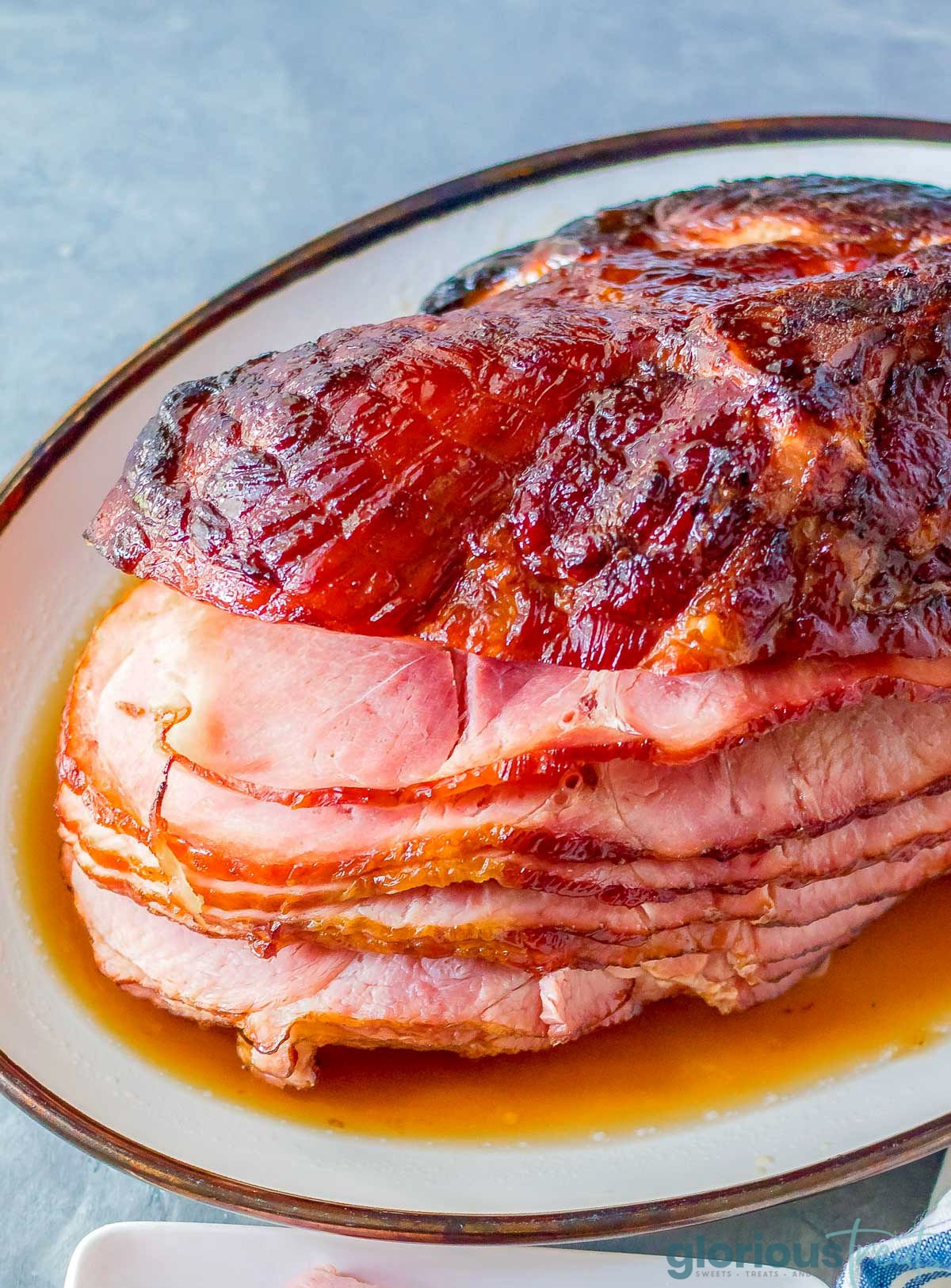 A ham on a white serving platter, with part of the ham cut into slices.