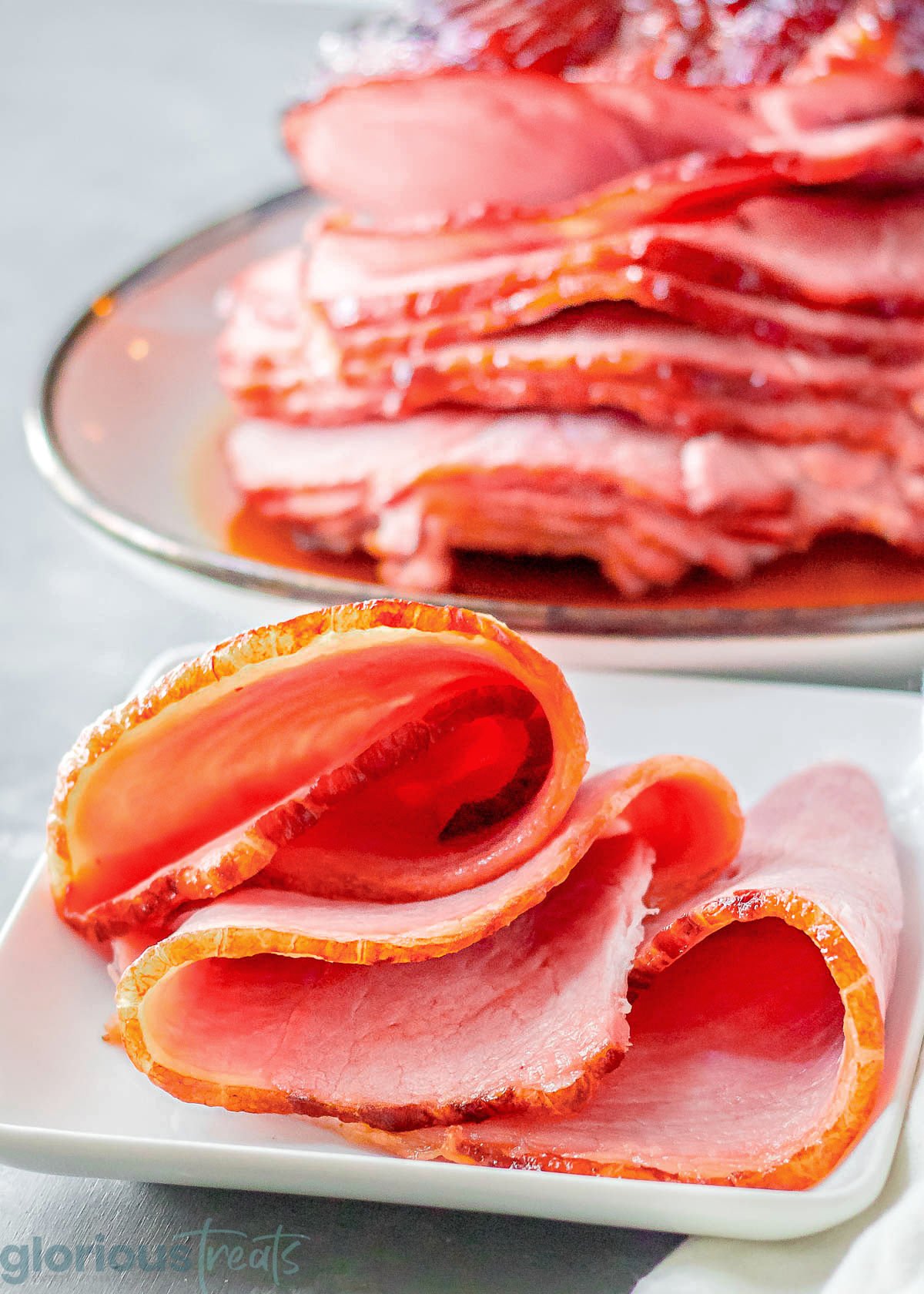 Sliced ham on a white plate with more ham on a platter in the background.