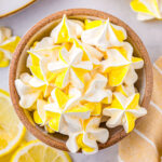 Top down view of lemon meringue cookies in a speckled bowl. Lemons and more cookies are scattered around the bowl.