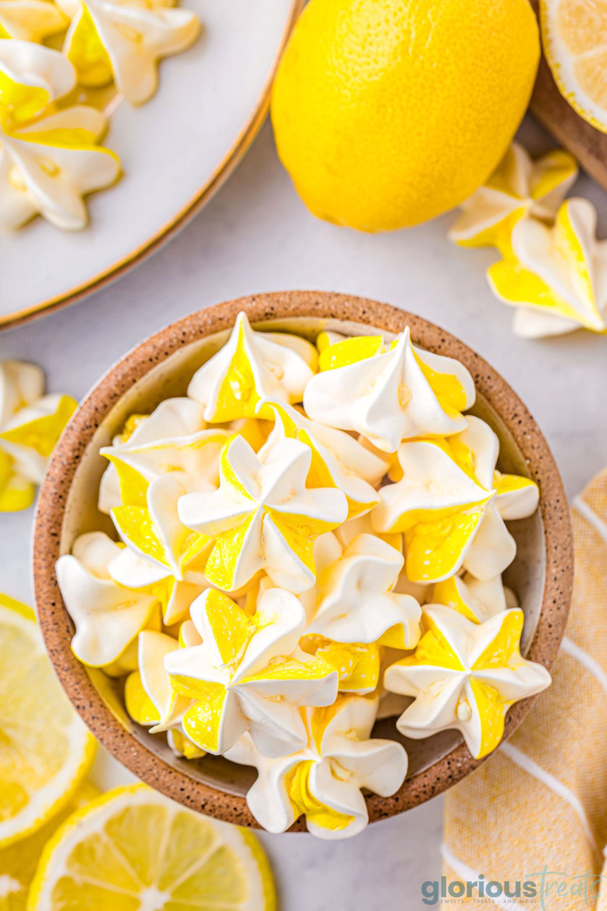 Top down view of lemon meringue cookies in a speckled bowl. Lemons and more cookies are scattered around the bowl.