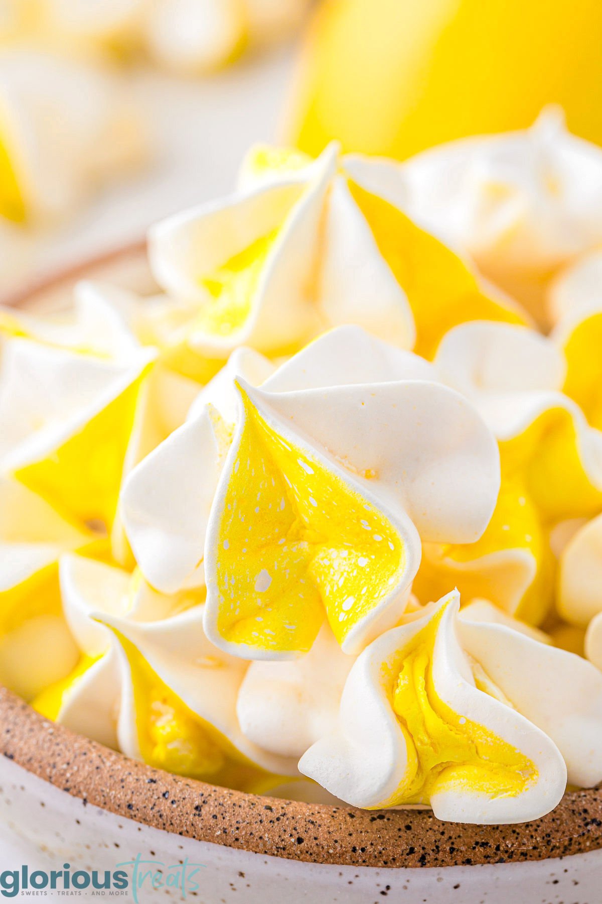 Close up view of lemon meringue cookies, to show the texture. The cookies are piled up in a speckled bowl.