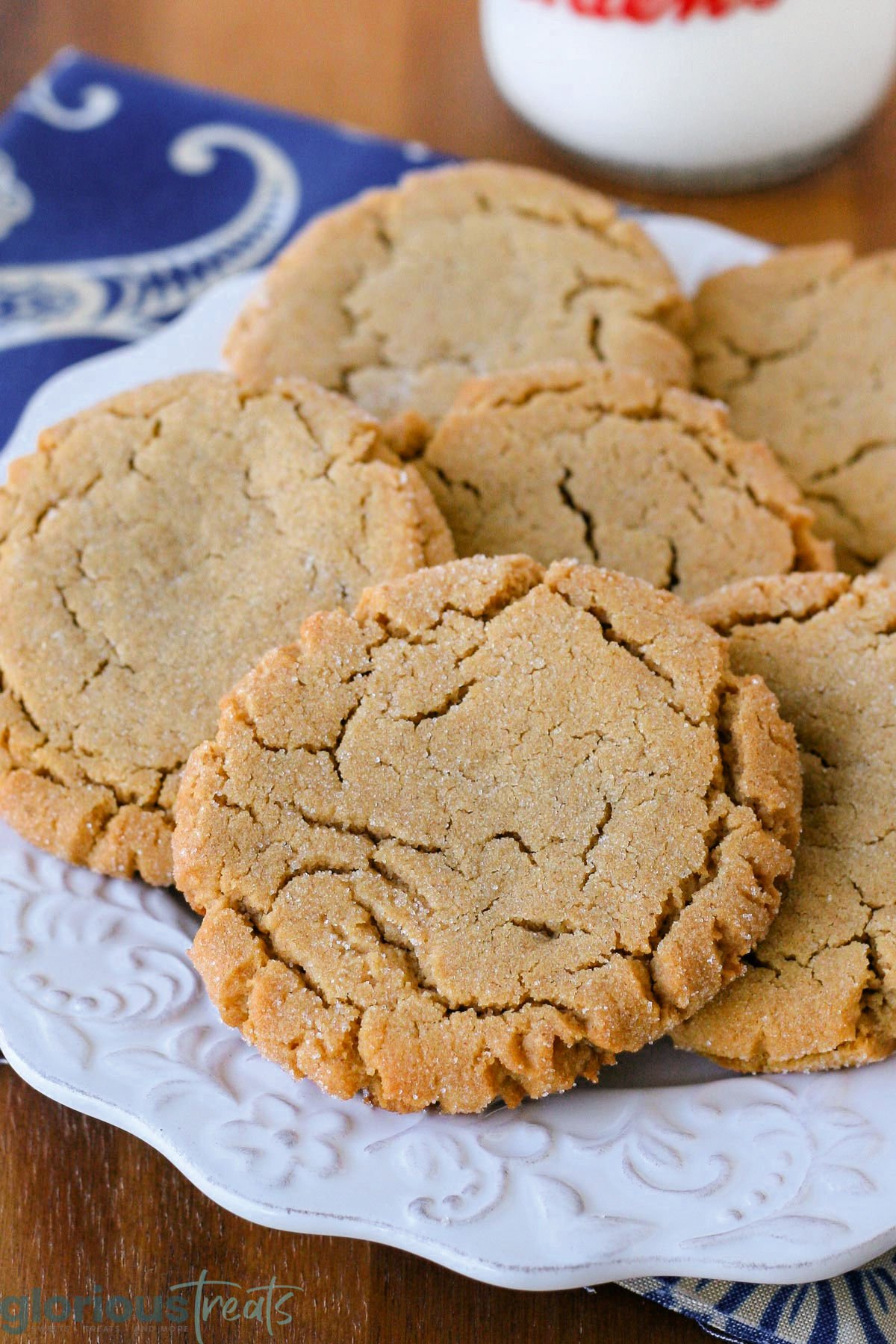 Close up of chewy peanut butter cookies stacked on a white round plate with scalloped edge.