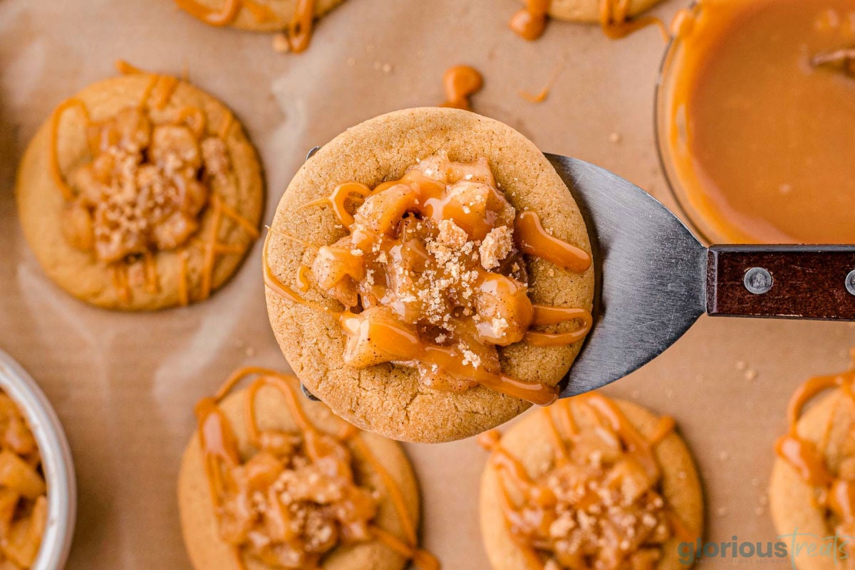 Apple caramel cookie being lifted with spatula over the rest of the cookies on a parchment paper.
