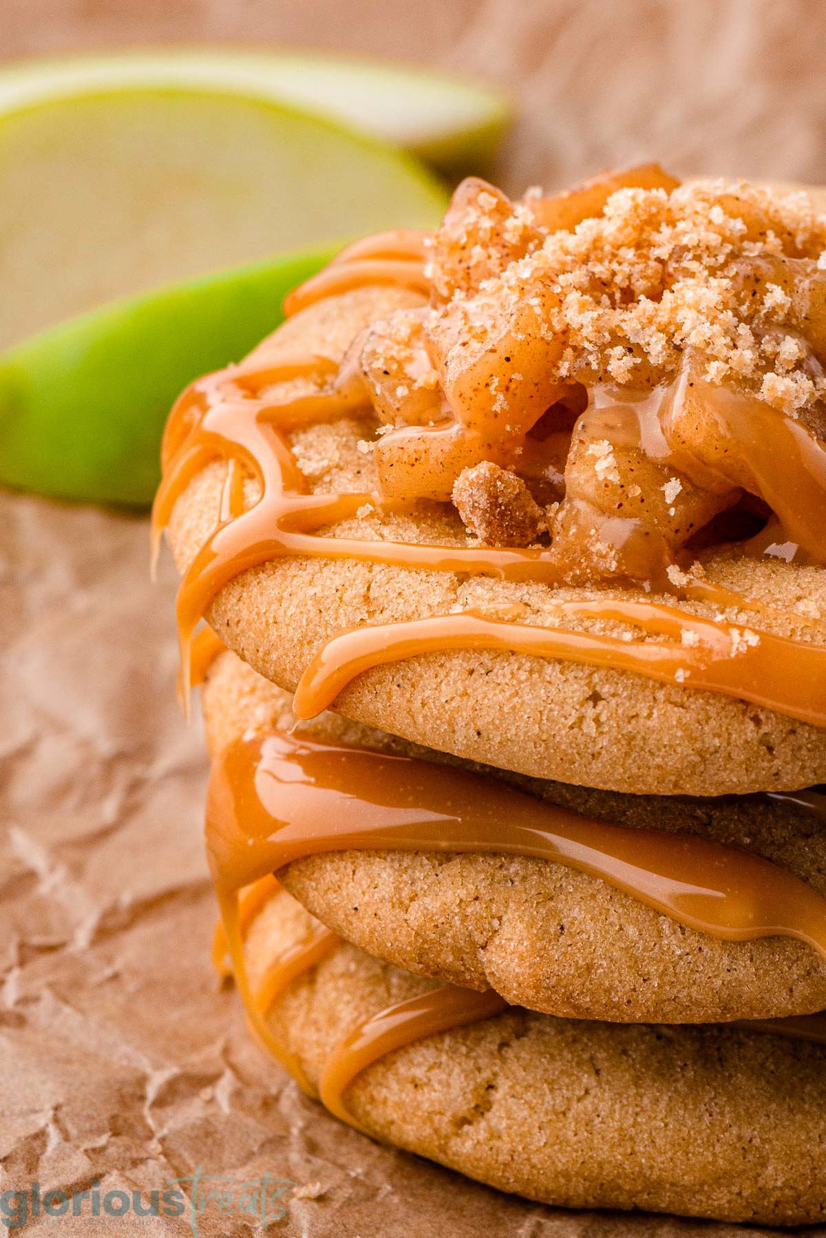 Close up look at caramel apple cookies recipe stacked three high on parchment. Green apple can be seen in the background.