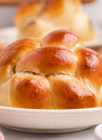 Shot of golden brown challah roll on white plate.