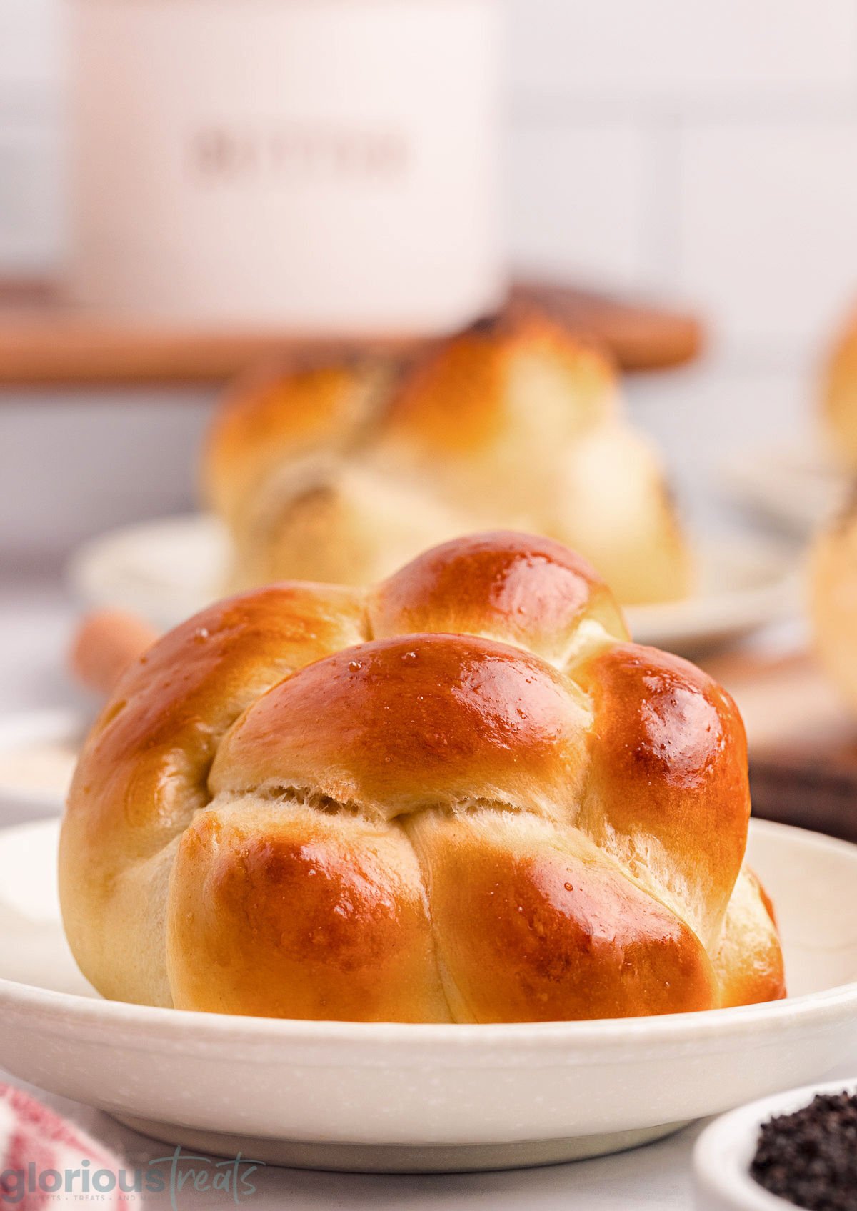 Shot of golden brown challah roll on white plate.