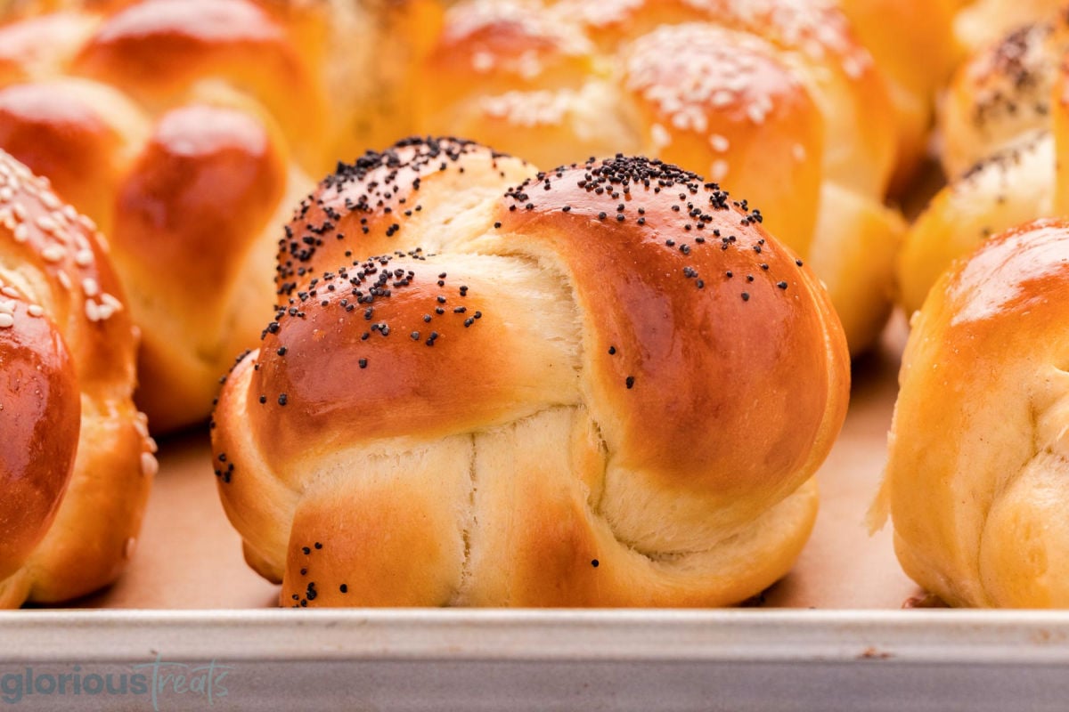 Wide shot of challah dinner roll with poppy seeds on baking sheet.