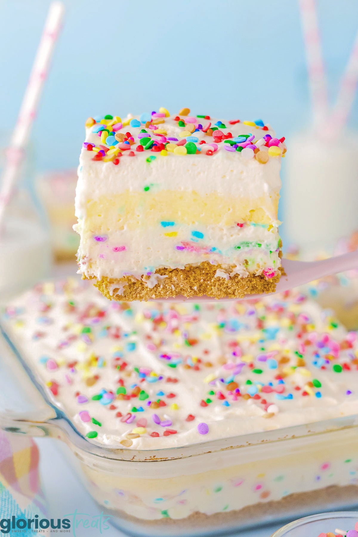 Piece of funfetti layered dessert being held up over the rest of the pan ready to serve.