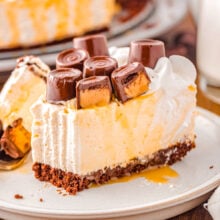 Slice of caramel cheesecake on small dessert plate topped with whipped cream and rolo candy.