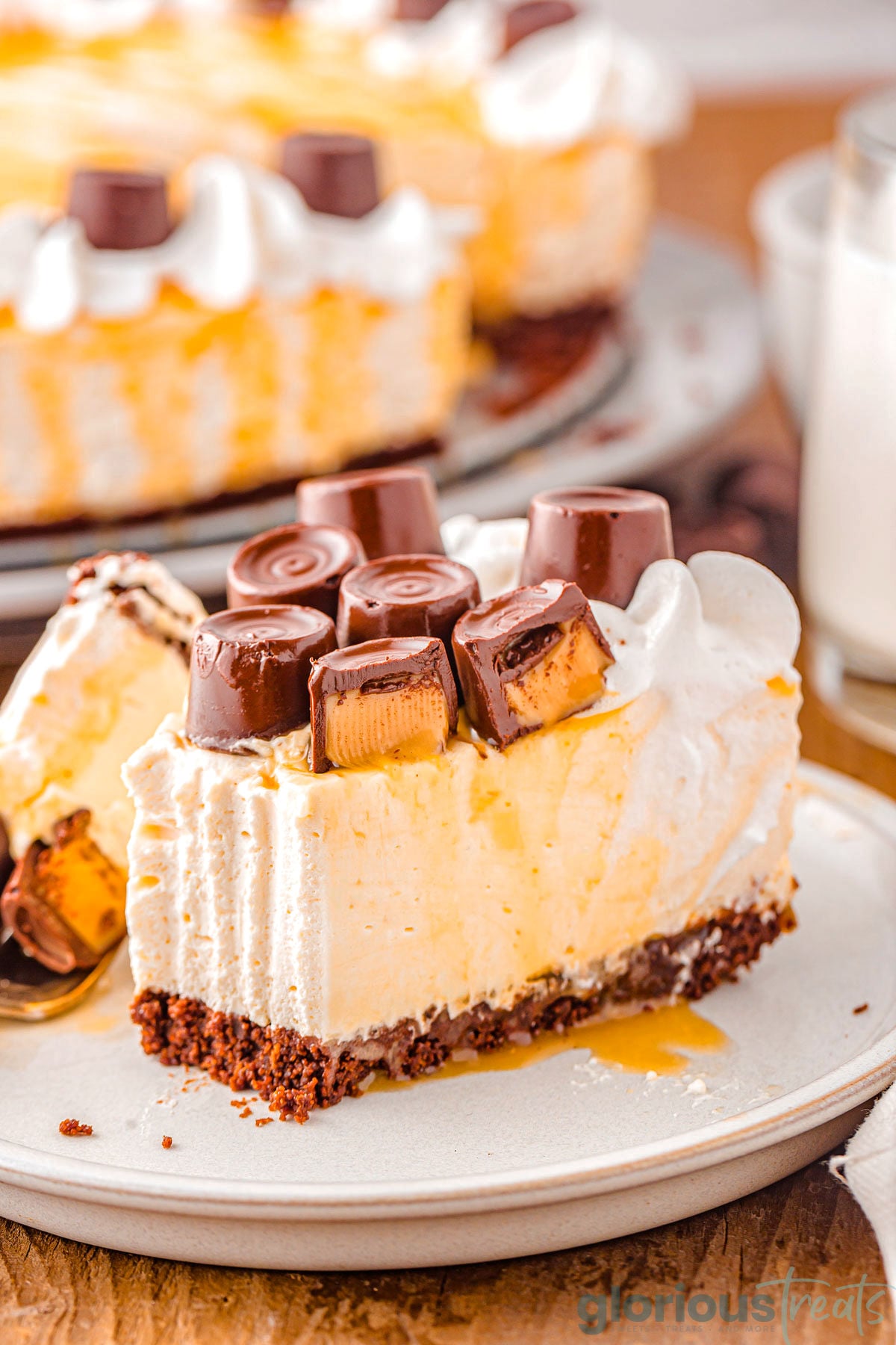 Slice of caramel cheesecake on small dessert plate topped with whipped cream and rolo candy.