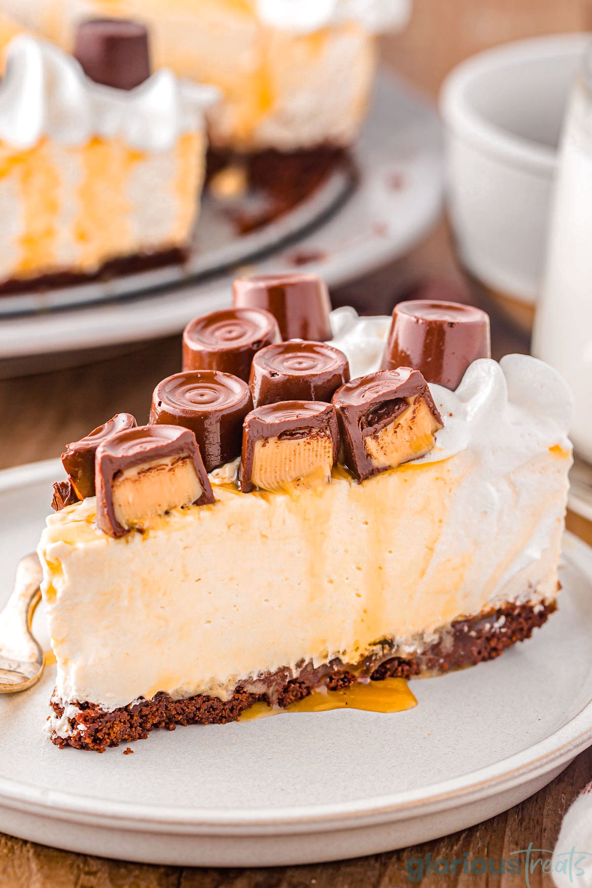 Slice of caramel cheesecake on small dessert plate topped with whipped cream and rolo candy.