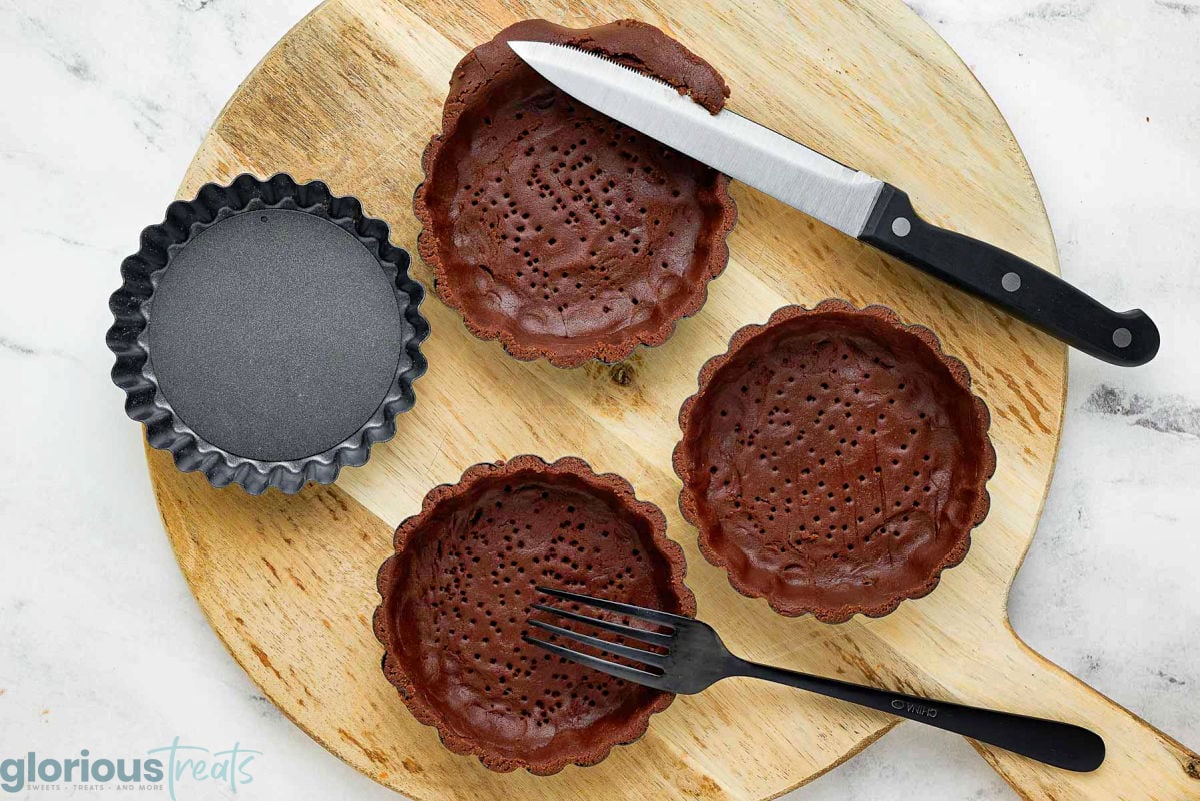 Wide shot of chocolate pastry shells being press into tartlet pans.
