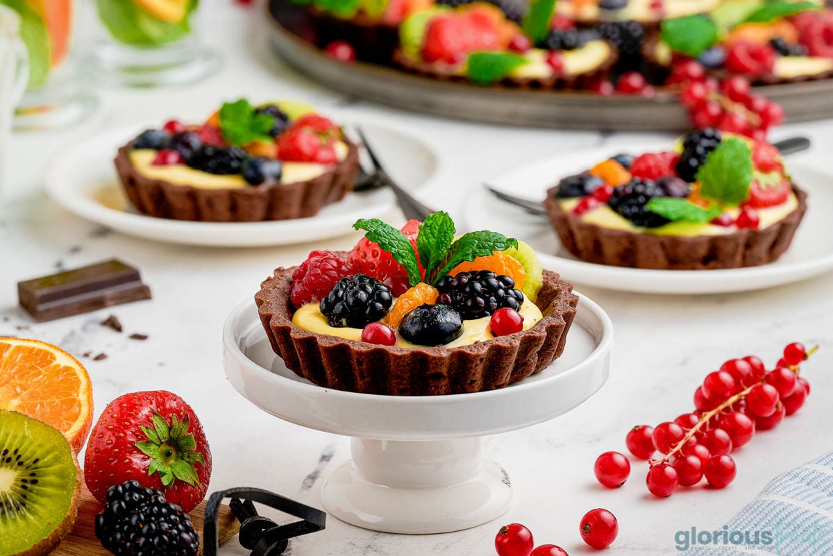 Wide shot of fresh fruit tart recipe served on chocolate tart shell and bright, colorful fruit.