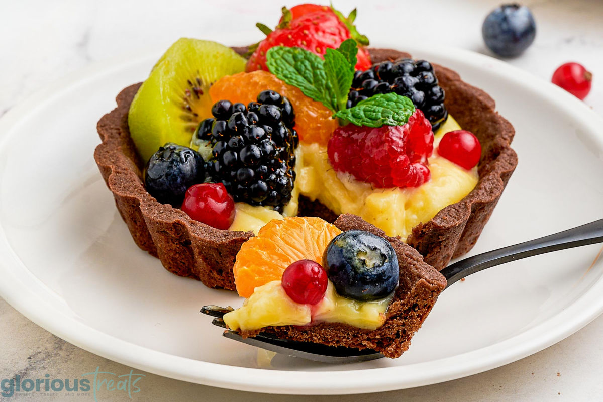 Wide shot of fork cutting into fruit tart with chocolate pastry.
