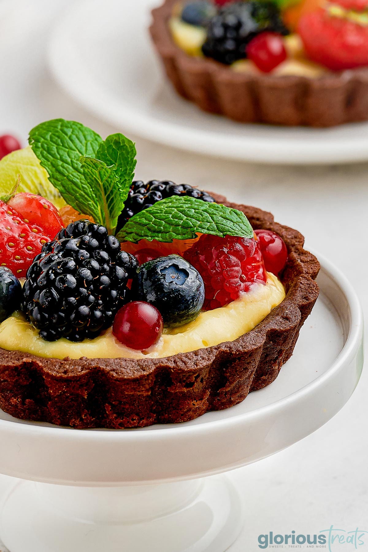 Close up shot of fruit tart with chocolate shell on on white cupcake stand.