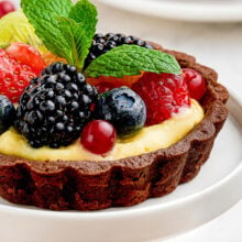 Close up shot of fruit tart with chocolate shell on on white cupcake stand.