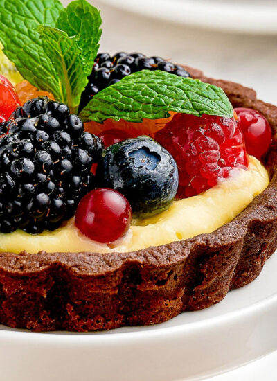 Close up shot of fruit tart with chocolate shell on on white cupcake stand.